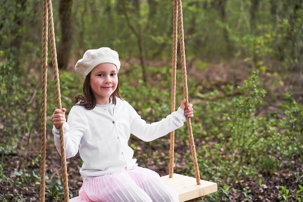 Una niña con una boina blanca monta un columpio en el bosque en autoaislamiento durante el coronavirus