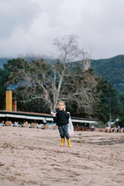 Una niña con una bolsa de basura mira alrededor de la playa.