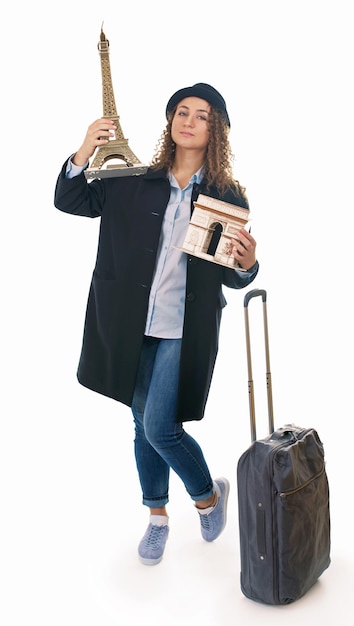 Foto niña con bolsa de viaje sostiene los símbolos de francia el modelo del arco triunfal y el arco triunfal sobre un fondo blanco