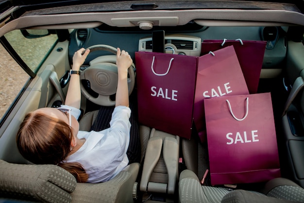 Una niña con bolsas de compras está conduciendo un automóvil, concepto de descuentos y compras, vista superior