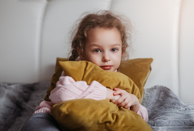 Niña bonita abraza una almohada amarilla en la cama