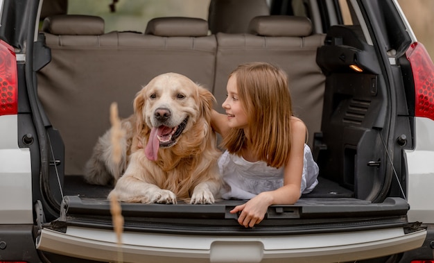 Niña bonita abrazando a un perro golden retriever y acostado juntos en el maletero del coche. Chico lindo niño descansando con mascota perrito en vehículo