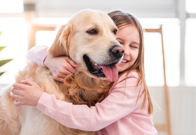 Foto niña bonita abrazando a un perro golden retriever y sonriendo. retrato de amistad