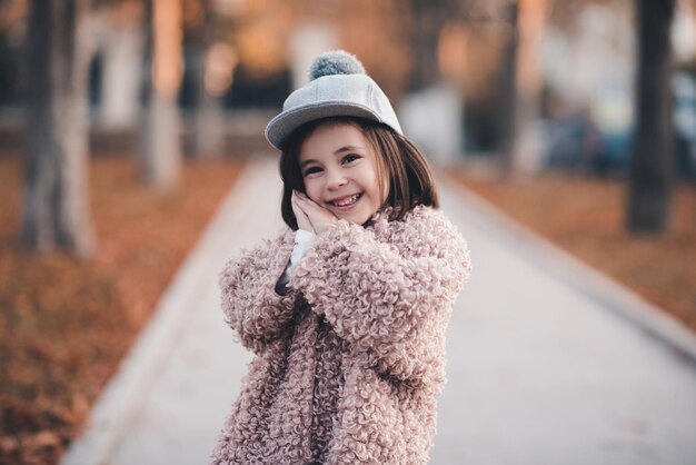 Niña bonita con abrigo de invierno y elegante sombrero posando en el parque