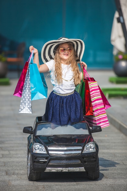 Niña bonita con bolsas de compras en un minicar