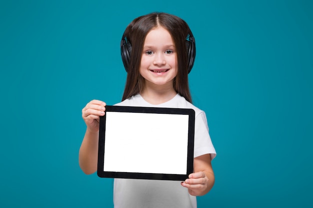 Niña bonita en camiseta y auriculares con tableta de fijación de pelo largo