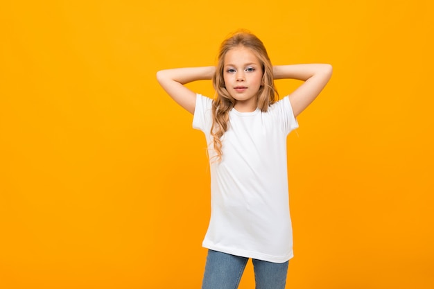 Niña bonita en camiseta blanca gesticulando y sonríe en la pared blanca