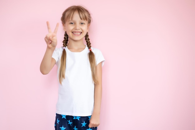 Niña bonita con una camiseta blanca sonriendo con un fondo rosa