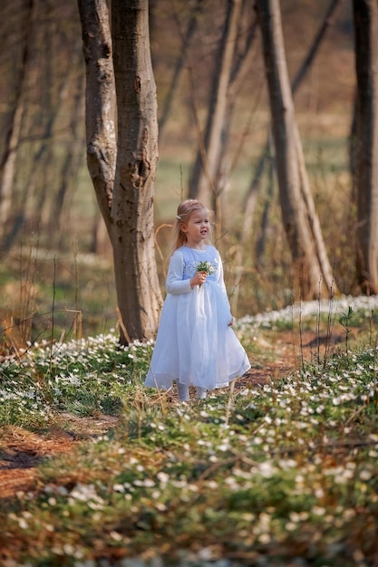 Niña bonita en un claro de campanillas de invierno Un niño camina en el bosque de primavera