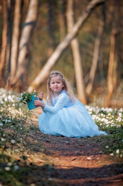 Niña bonita en un claro de campanillas de invierno Un niño camina en el bosque de primavera