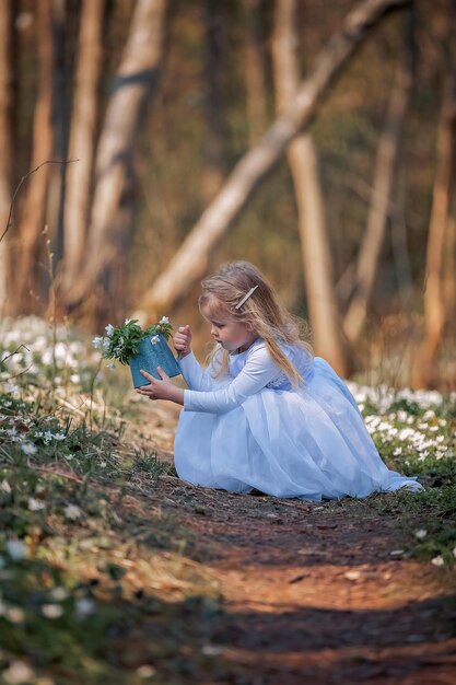 Niña bonita en un claro de campanillas de invierno Un niño camina en el bosque de primavera