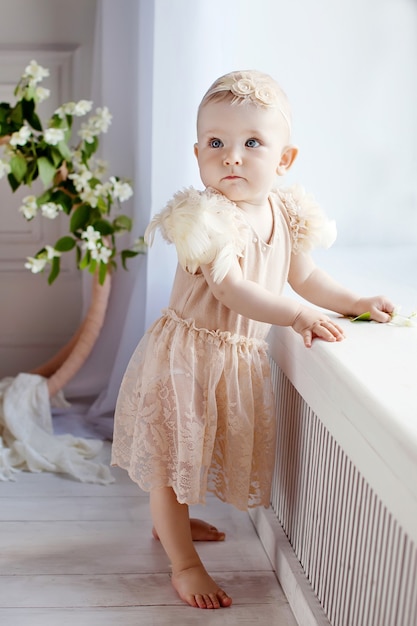 Niña bonita descalza está junto a la ventana. Preciosa niña de 1 año da los primeros pasos