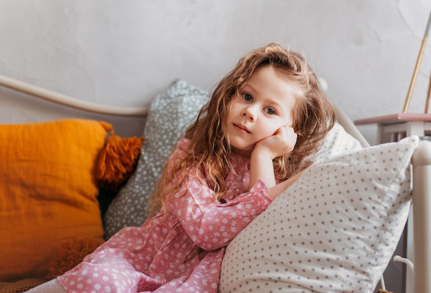 Una niña bonita descansa sobre una almohada en una cama en el dormitorio de los niños. Reflexión y ensoñación