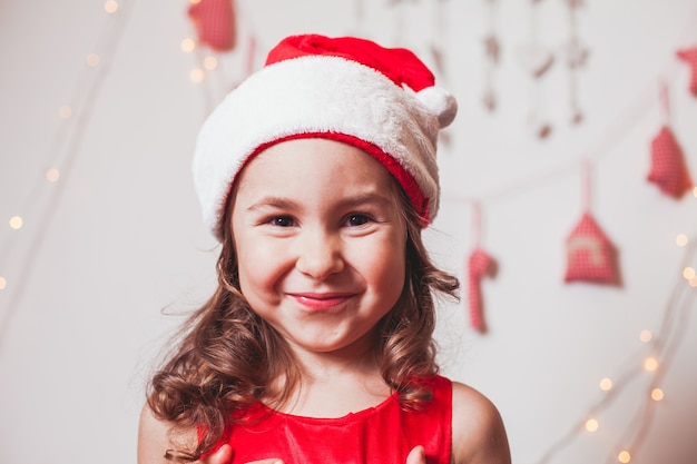 Niña bonita con un gorro de santa claus está decorando el árbol de navidad