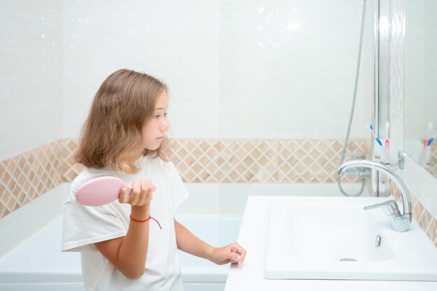 Una niña bonita con grandes ojos azules y un peine en la mano el niño peina el cabello rebelde lindo