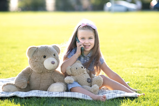 Niña bonita hablando por teléfono móvil sonriendo felizmente al aire libre en verano.