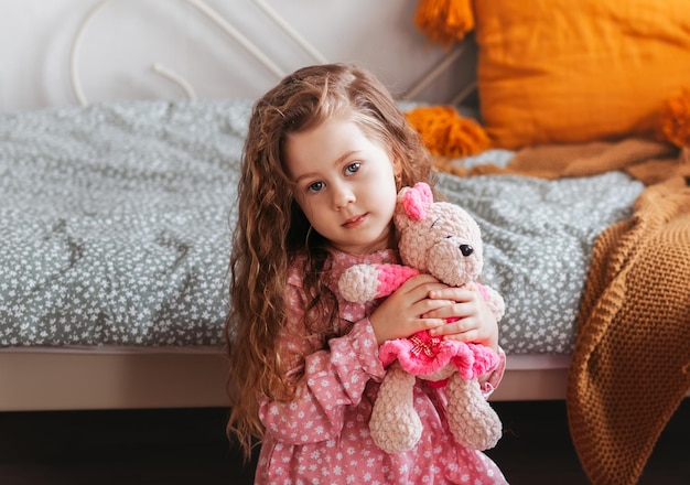 Niña bonita juega con oso de peluche en el dormitorio de los niños