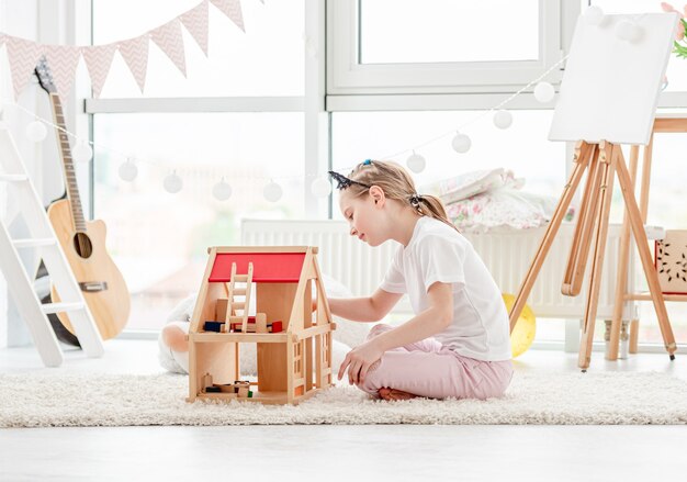 Niña bonita jugando con casa de muñecas