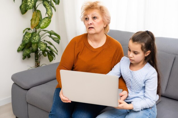 niña bonita jugando la computadora portátil de su abuela en casa.