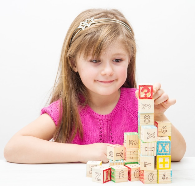 Niña bonita jugando con cubos de madera con letras y números