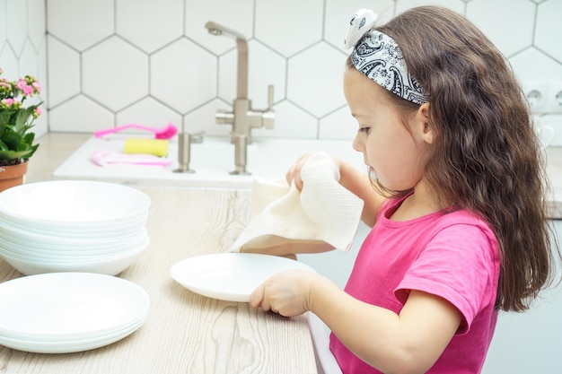 Niña bonita limpiando platos blancos transparentes con una toalla seca en el juego de cocina Vajilla seca después del lavado