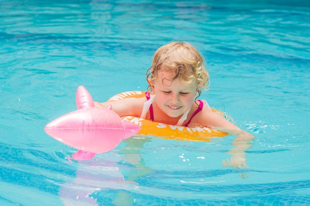 Niña bonita nadando en la piscina al aire libre y divertirse con un círculo inflable