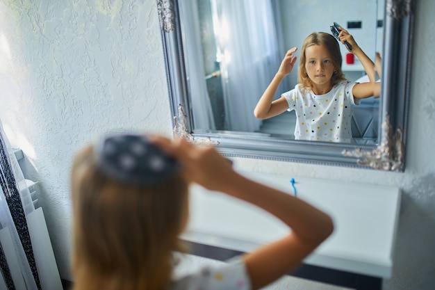 Foto niña bonita peinando ella misma el cabello delante de un espejo