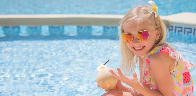 Niña bonita en la piscina bebiendo jugo