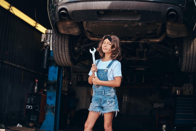 La niña bonita posa para el fotógrafo con una herramienta en el taller de autoservicio.