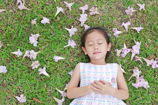 Niña bonita que duerme en hierba verde con la flor del rosa de la caída en el jardín al aire libre.