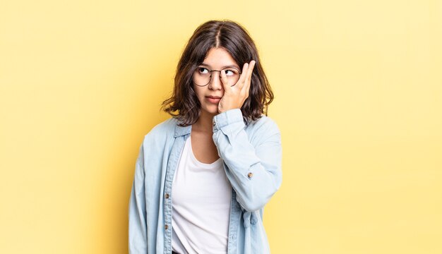 Niña bonita que se siente aburrida, frustrada y con sueño después de una tarea tediosa, aburrida y tediosa, sosteniendo la cara con la mano