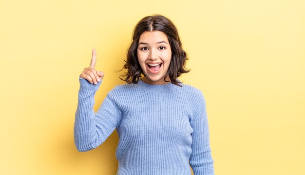 Niña bonita que se siente como un genio feliz y emocionado después de darse cuenta de una idea, levantando alegremente el dedo, ¡eureka!