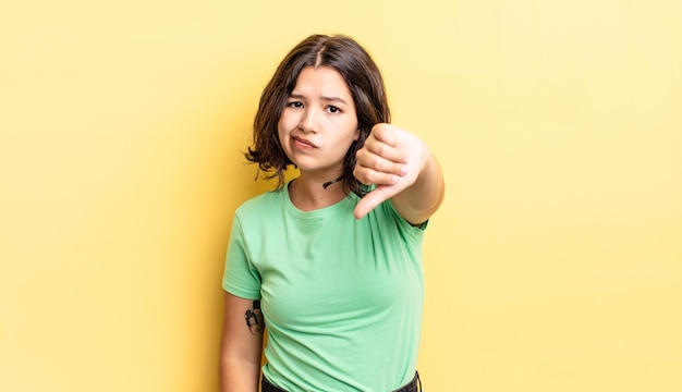 Niña bonita que se siente enfadada, enojada, molesta, decepcionada o disgustada, mostrando los pulgares hacia abajo con una mirada seria.