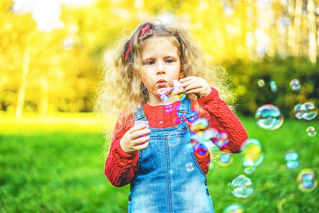 Niña bonita que sopla burbujas en el parque.