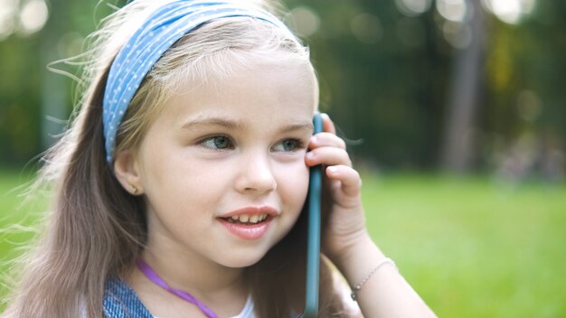 Niña bonita que tiene conversación en su teléfono móvil en el parque de verano.