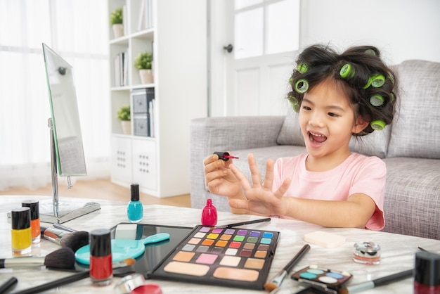 niña bonita que usa los cosméticos y esmaltes de uñas de mamá cuando su mamá no está en casa