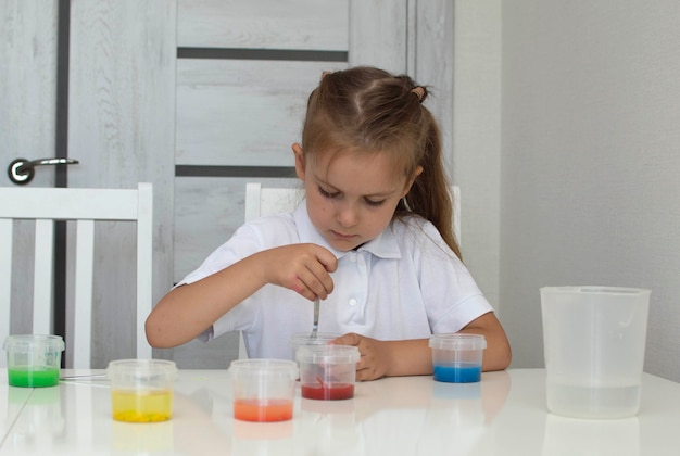 Una niña bonita realiza experimentos físicos con agua en casa. Un niño agrega productos químicos a un experimento con agua coloreada.