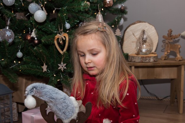 Una niña bonita con regalos de Navidad sentado junto al árbol de Navidad en la habitación, concepto de Año Nuevo