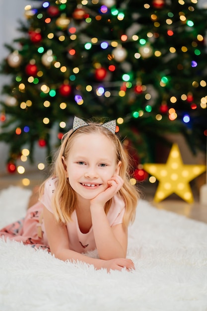 Niña bonita rubia en vestidos rosados en el árbol de navidad