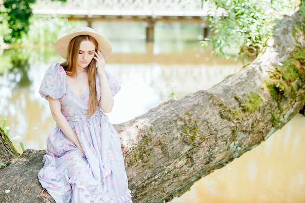 una niña bonita se sienta en el borde de un árbol junto al río y mira hacia otro lado