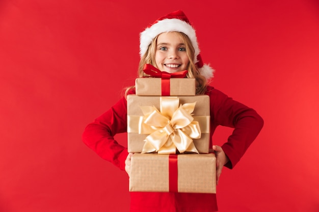 Niña bonita con sombrero de Navidad que se encuentran aisladas, sosteniendo la pila de cajas presentes