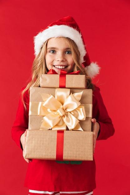 Niña bonita con sombrero de Navidad que se encuentran aisladas, sosteniendo la pila de cajas presentes