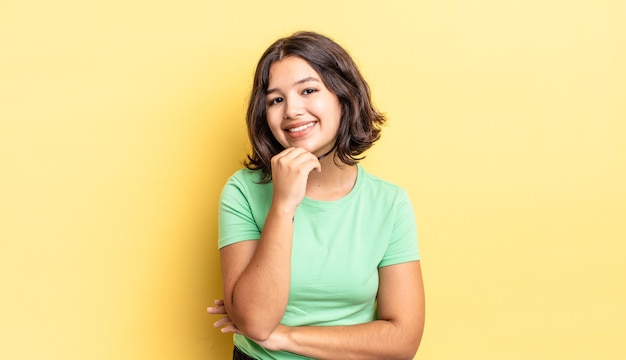 Niña bonita sonriendo, disfrutando de la vida, sintiéndose feliz, amigable, satisfecho y despreocupado con la mano en la barbilla