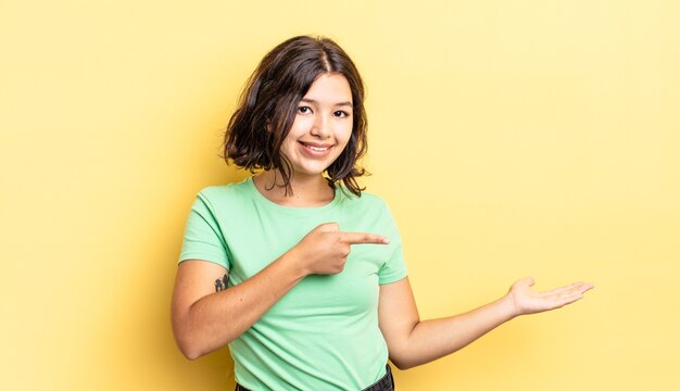 Niña bonita sonriendo, sintiéndose feliz, despreocupada y satisfecha, señalando el concepto o la idea en el espacio de la copia en el lateral