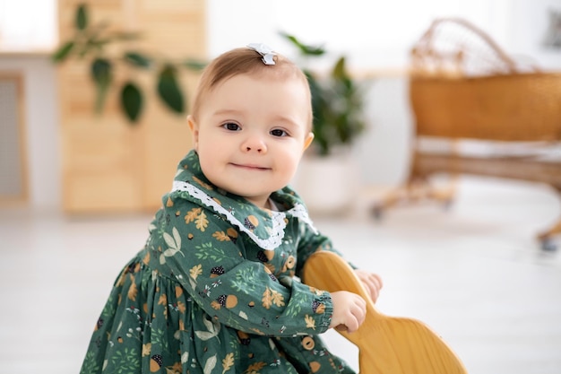 Una niña bonita con un vestido de algodón verde está sentada en un caballo mecedor en la sala de estar de la casa mirando a la cámara sonriendo un gran retrato