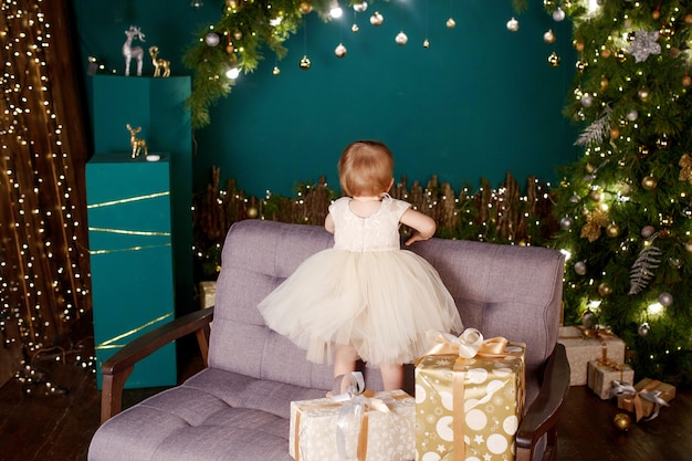 Niña bonita en vestido blanco mirando el árbol de Navidad y las luces.