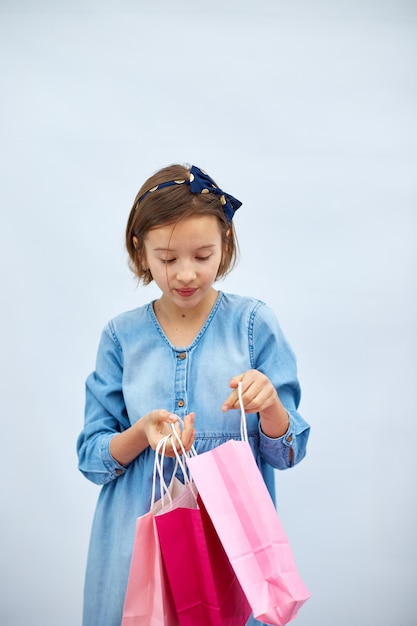 Niña bonita en vestido de mezclilla informal con bolsas de compras rosa en la mano