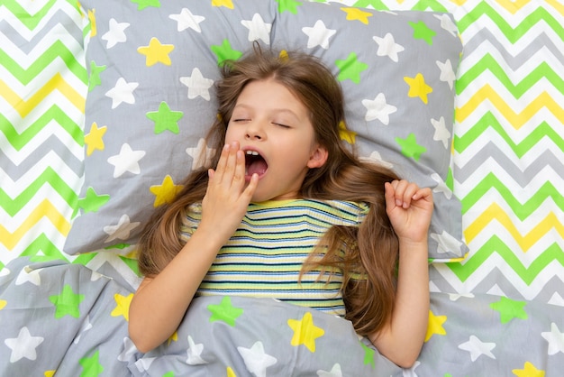 Una niña bosteza por la mañana acostada en la cama.