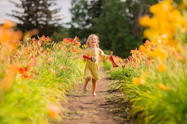 niña con botas de goma roja y un sombrero de paja regando flores rojas de riego en el jardín