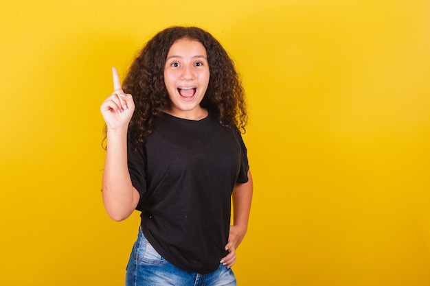 Foto niña brasileña latinoamericana para cabello afro fondo amarillo expresión de idea sugerencia creativa idea i indicación de saber la respuesta dedo índice levantado